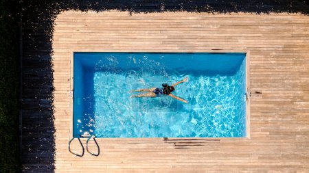 Foto de Drone ver longitud completa de la mujer irreconocible con el pelo largo húmedo oscuro flotando en la piscina al aire libre en el día soleado en el complejo tropical - Imagen libre de derechos