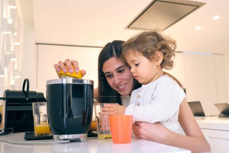 Photo for Happy young woman and little child preparing delicious fruit juice using electric juicer for breakfast in kitchen at home - Royalty Free Image