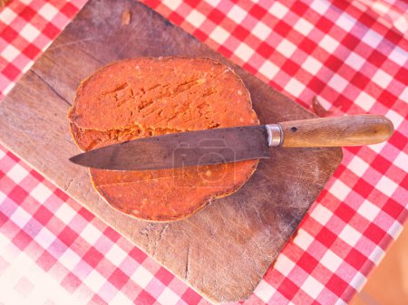 Photo for Top view half of appetizing fresh Spanish sobrassada sausage prepared with pork and paprika placed on wooden cutting board with knife on table - Royalty Free Image