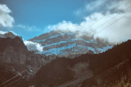 Téléchargez les photos : Falaises rocheuses rugueuses couvertes de givre blanc situé en terrain montagneux avec des arbres et des lignes électriques par temps froid d'hiver - en image libre de droit
