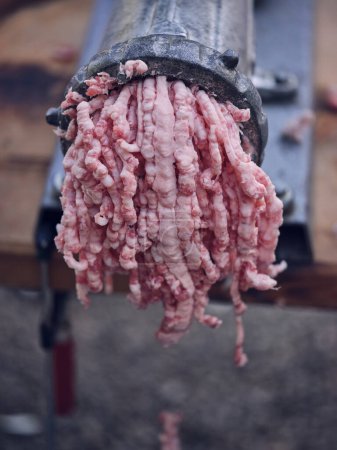 Photo for From above of closeup of raw minced meat getting from metal manual grinder placed on wooden table in village of Mallorca while preparing traditional meal - Royalty Free Image
