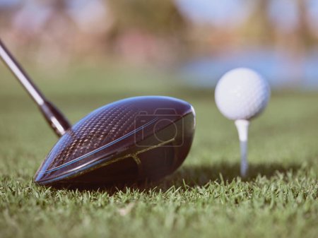 Foto de Primer plano del club de golf negro cerca de la pelota de golf blanca en el pequeño puesto colocado en el césped verde herboso del campo de golf a la luz del sol - Imagen libre de derechos