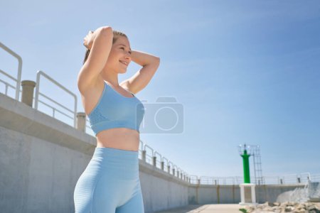 Photo for Side view of young sincere female athlete in sportswear with hands behind head looking forward during break from workout - Royalty Free Image