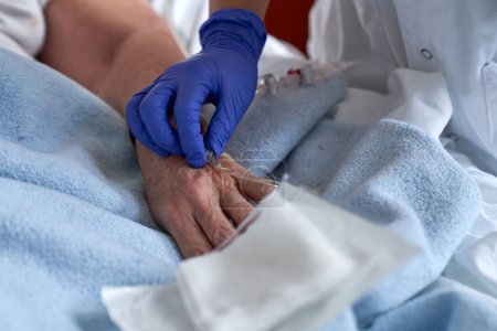 Foto de Médico anónimo de cultivo en guantes de látex insertando catéter para fluido intravenoso en la mano del paciente sin rostro durante el procedimiento en el hospital - Imagen libre de derechos