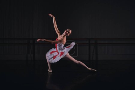 Foto de Cuerpo completo de bailarina sensual en traje escénico y tutú bailando papel de ballet mientras ensayan en estudio oscuro - Imagen libre de derechos