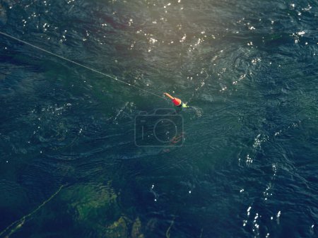 Photo for From above striped fishing float with line on surface of clear river water on sunny day in nature - Royalty Free Image