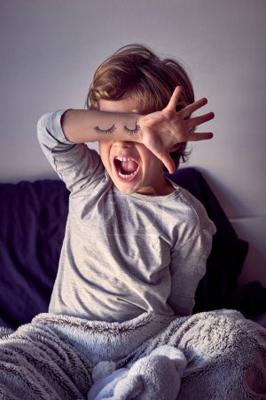 Foto de Lindo niño cubriendo los ojos con la mano, boca abierta. ojos pintados en la mano - Imagen libre de derechos