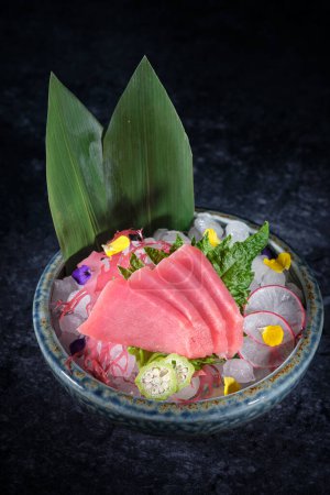 Téléchargez les photos : Bol au délicieux sashimi au filet de poisson frais et radis et citron vert placé sur de la glace décorée de feuilles de banane - en image libre de droit