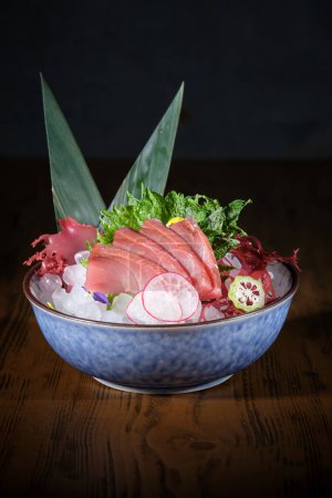 Foto de Cuenco con delicioso sashimi con filete de pescado fresco y rábano y lima colocados en el hielo decorado con hojas de plátano - Imagen libre de derechos