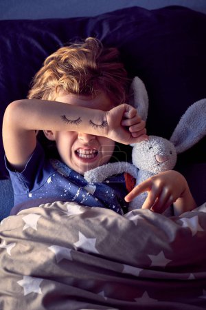 Photo for Little boy covering eyes with hand. painted eyes on hand, sleepy child with bunny toy - Royalty Free Image