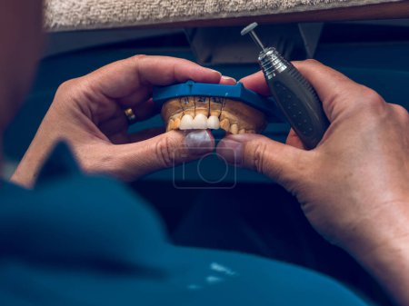Foto de Desde arriba de la cosecha anónimo especialista en machos moliendo falsos dientes de cerámica colocados en la mandíbula fundida mientras se hace la prótesis en el laboratorio - Imagen libre de derechos