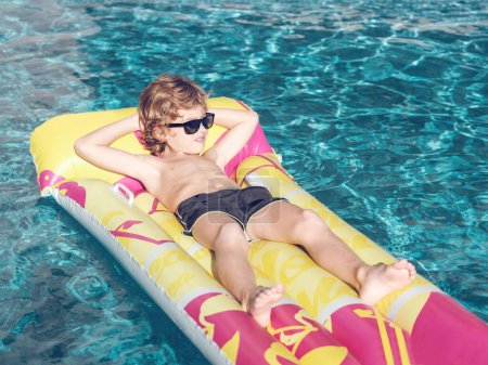 Foto de Chico relajado sin camisa con las manos detrás de la cabeza mirando hacia otro lado mientras está acostado en flotador inflable en la piscina limpia en el día soleado en Mallorca, España - Imagen libre de derechos