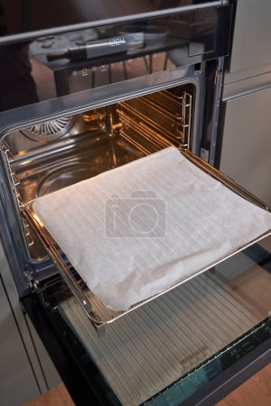 Foto de Desde arriba de la estufa de metal brillante con bandeja para hornear vacía abierta y lista para cocinar - Imagen libre de derechos