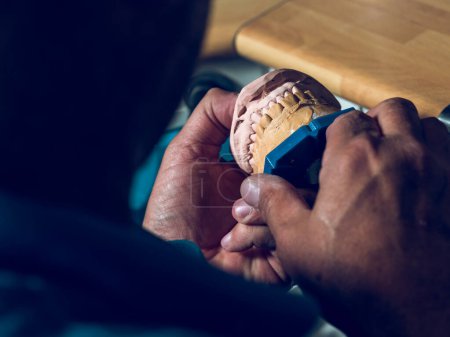 Téléchargez les photos : Grand angle de culture technicien dentaire méconnaissable tenant la mâchoire artificielle dans les mains près de la table de travail - en image libre de droit