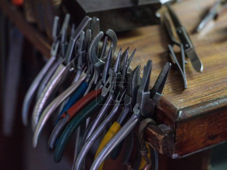 Photo for From above of pliers hanging in row on side of wooden table in jewelry workshop - Royalty Free Image
