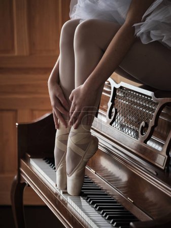Foto de Alto ángulo de cultivo femenino anónimo bailarina de ballet sentado en la parte superior del piano y pulsando las teclas con los pies en zapatos de punta - Imagen libre de derechos