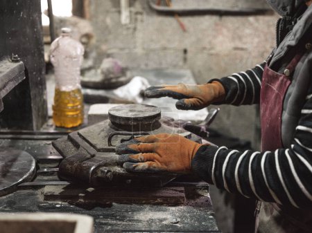 Téléchargez les photos : Vue latérale de la récolte travailleur masculin méconnaissable dans des gants de protection et tablier de travail avec moule en métal pour la fabrication de carreaux en atelier - en image libre de droit