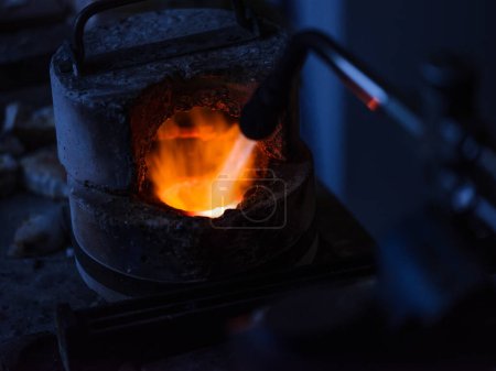 Téléchargez les photos : Angle élevé de torche à gaz en cours d'exécution liquéfiant le métal dans un four rond dans un atelier sombre - en image libre de droit
