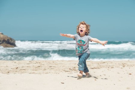 Foto de Cuerpo completo de chico activo juguetón en ropa casual corriendo en la costa arenosa cerca del mar ondulante mientras se divierten en la naturaleza - Imagen libre de derechos