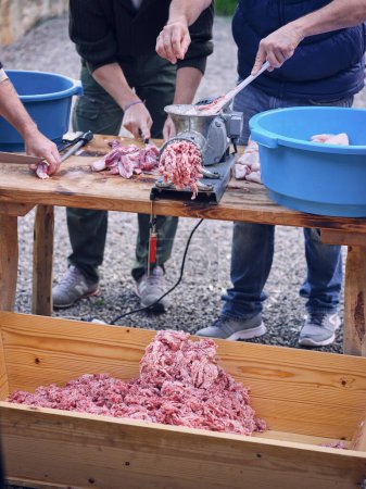 Téléchargez les photos : Cultiver boucher mâle méconnaissable dans des vêtements décontractés debout à la table en bois ensemble et broyage de bœuf cru avec hachoir à viande dans l'abattoir traditionnel espagnol - en image libre de droit