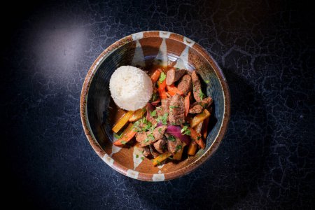 Foto de Vista superior de deliciosa comida de carne de res salteada con verduras hervidas y arroz cocido servido en tazón de cerámica sobre fondo negro - Imagen libre de derechos