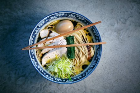 Téléchargez les photos : Vue du dessus de savoureuse soupe de nouilles japonaises avec oeuf bouilli et algues dans le bouillon sous les bâtonnets de nourriture sur le bol - en image libre de droit