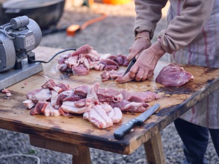 Photo for From above of unrecognizable person slicing raw meat with sharp knife on wooden table while preparing traditional Spanish delicacy in Matanza in Mallorca - Royalty Free Image
