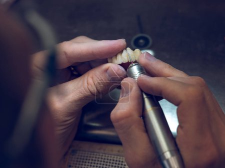 Photo for From above of crop anonymous male dental specialist shaping fake ceramic teeth using grinder while making denture in modern laboratory - Royalty Free Image