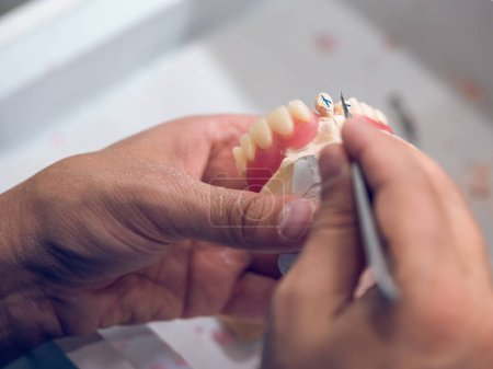 Téléchargez les photos : De dessus de la culture méconnaissable spécialiste dentaire masculin sculpter des dents en céramique artificielle à l'aide d'un outil métallique tranchant tout en travaillant dans un laboratoire dentaire - en image libre de droit