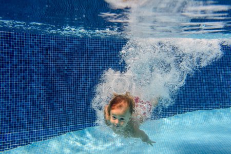Téléchargez les photos : Adorable petit garçon plongeant avec éclaboussures et bulles et nageant sous l'eau dans la piscine - en image libre de droit