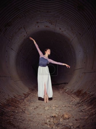 Foto de Cuerpo completo de talentosa bailarina de ballet femenina en zapatos puntiagudos bailando con brazo levantado en viejo túnel con paredes erosionadas - Imagen libre de derechos