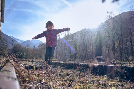 Photo for Full body of boy outstretching arms while balancing on rail track among leafless trees in sunny day in highland - Royalty Free Image