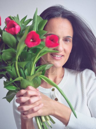 Téléchargez les photos : Portrait de femme brune heureuse debout sur fond blanc avec le sourire et les yeux fermés tenant tas de tulipes - en image libre de droit