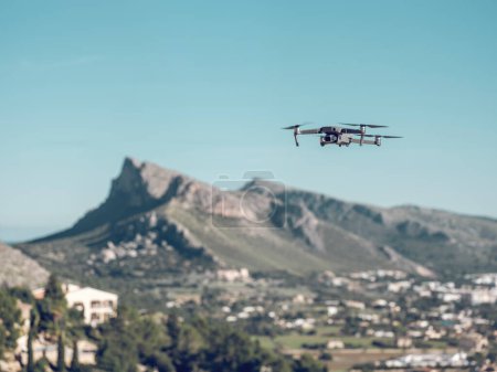 Foto de Drone contemporáneo volando sobre fondo borroso de pico de montaña y cielo azul sobre la ciudad de Pollensa en Mallorca, España - Imagen libre de derechos