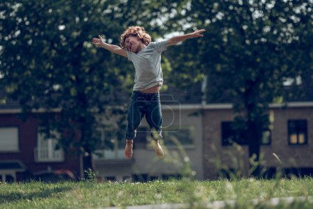 Photo for Full body of barefoot joyful preteen boy jumping in green meadow in summer day in countryside - Royalty Free Image