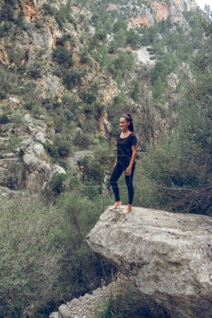 Téléchargez les photos : Pieds nus touriste en vêtements noirs debout sur la pierre contre la chaîne de montagnes et les buissons le jour de l'été dans les hauts plateaux de Majorque, Espagne - en image libre de droit