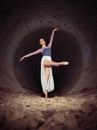 Photo for Full body of graceful female ballet dancer in pointe shoes raising leg while dancing with raised arm in shabby tunnel - Royalty Free Image