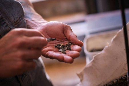 Foto de Cosecha irreconocible trabajador masculino sosteniendo pequeñas piezas de metal durante el trabajo en taller de soldadura profesional en el día - Imagen libre de derechos
