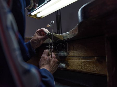 Foto de Artesano de cultivo anónimo con detalle de metal de procesamiento de sierra de joyería mientras trabaja en taller oscuro - Imagen libre de derechos