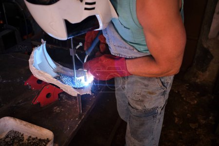 Photo for High angle of anonymous male technician in protective helmet working on metal details at workbench in garage using welding torch - Royalty Free Image