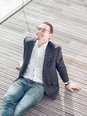 Téléchargez les photos : D'en haut de gai gestionnaire masculin bien habillé dans des lunettes assis sur la rue en bois et levant les yeux - en image libre de droit