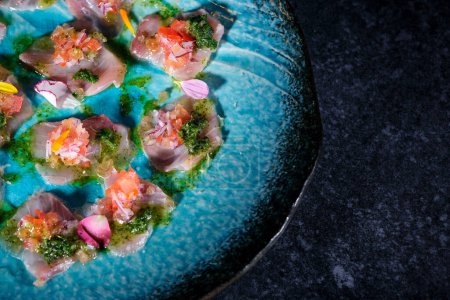 Téléchargez les photos : Vue de dessus de délicieuses bouchées de poisson avec sauce et légumes fleuris en sauce bleue sur une assiette placée sur un fond de table en marbre foncé - en image libre de droit