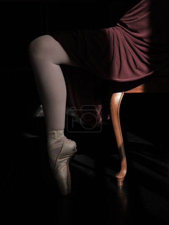 Photo for Side view of crop anonymous female ballerina in elegant dress sitting on chair and standing on tiptoe in pointe shoes - Royalty Free Image