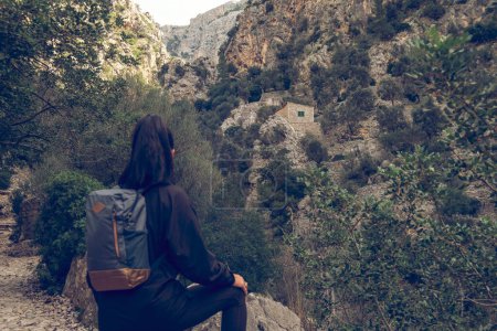 Photo for Back view of unrecognizable woman tourist with backpack resting on edge of hill cliff white traveling to Biniaraix village of Soller region in Mallorca - Royalty Free Image