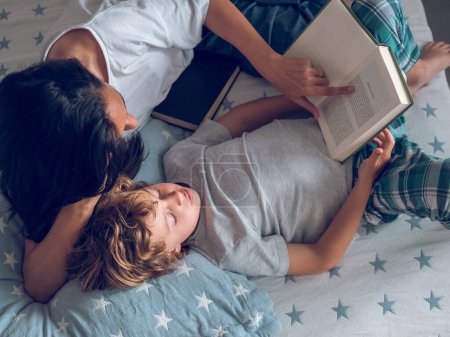 Téléchargez les photos : Top vue de preteen garçon et maman lecture livre intéressant tout en étant couché sur le lit - en image libre de droit