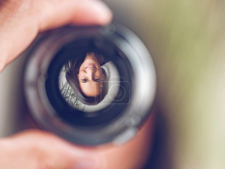 Photo for Closeup of crop hand holding lens with upside down reflection of smiling female with long dark hair looking at camera against blurred background - Royalty Free Image