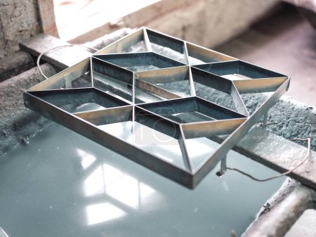 Téléchargez les photos : D'en haut de nouveau moule en métal avec ornement géométrique placé sur une étagère en bois au-dessus du récipient avec de l'eau dans un atelier artisanal de tuiles artisanales - en image libre de droit
