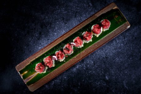 Photo for Top view of delicious uramaki sushi lump with toppings of raw tuna served on smooth wooden dark table - Royalty Free Image