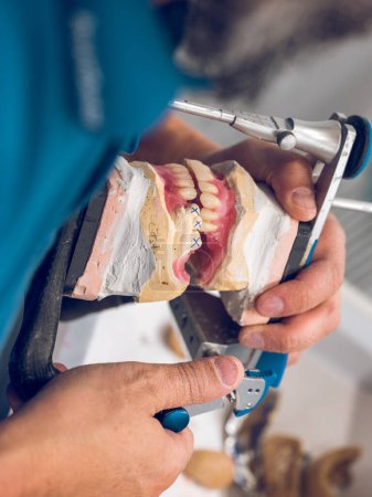 Téléchargez les photos : De dessus de culture orthodontiste mâle anonyme mettre la mâchoire de prothèse dans l'articulateur tout en faisant des implants en laboratoire dentaire - en image libre de droit