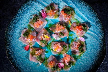 Foto de Vista superior de deliciosos bocados de pescado con salsa y verduras floridas en salsa azul en el plato colocado sobre fondo de mesa de mármol oscuro - Imagen libre de derechos